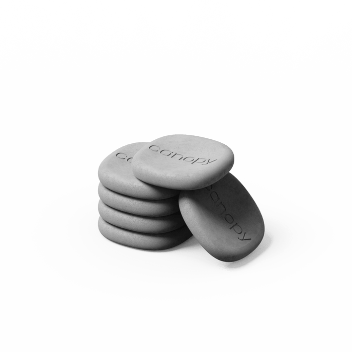 Aroma Stone 6-Pack featuring smooth gray ceramic discs stacked together with engraved text, designed for essential oil diffusion and aromatherapy use. Minimalist black and white product photography against white background.