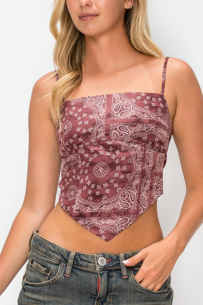 A woman wearing a dusty rose and white paisley bandana print crop top with spaghetti straps, paired with blue jeans, against a plain white background.