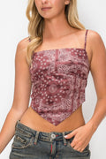 A woman wearing a dusty rose and white paisley bandana print crop top with spaghetti straps, paired with blue jeans, against a plain white background.