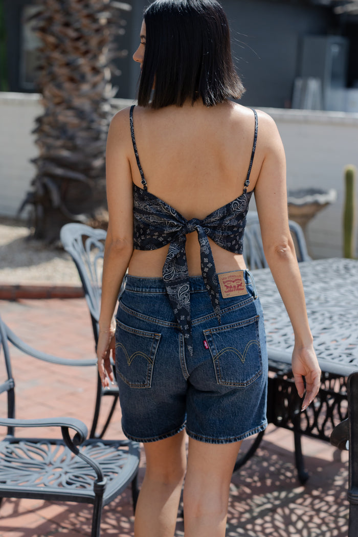 Woman wearing a patterned top and denim shorts on a patio.