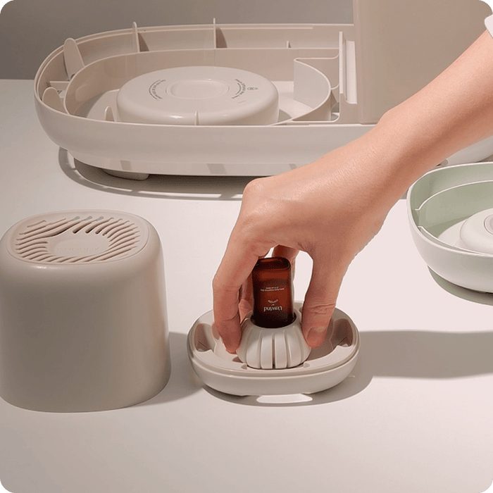 Hand placing an essential oil bottle into a white ceramic Diffusion Well 3-Pack, shown on a dark wooden table next to a terracotta plant pot, demonstrating the simple setup process for long-lasting aromatherapy by Canopy