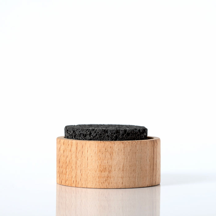 A round, black Plant Therapy Lava Rock Passive Diffuser rests on a light wooden holder, displayed against a white background.