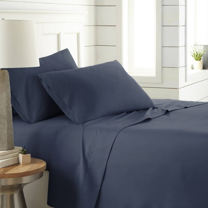 Angled view of Southshore Essentials 4-piece sheet set in navy blue showcasing smooth ultra-soft fabric and two pillowcases on a white paneled bedside background