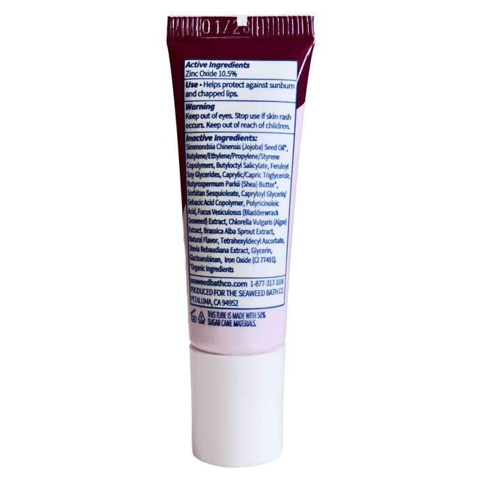 A tube of The Seaweed Bath Co Tinted Mineral Lip Shine SPF 20, featuring visible ingredient and warning labels, a white cap, and maroon-and-white packaging—formulated with nourishing shea butter—standing upright against a white background.