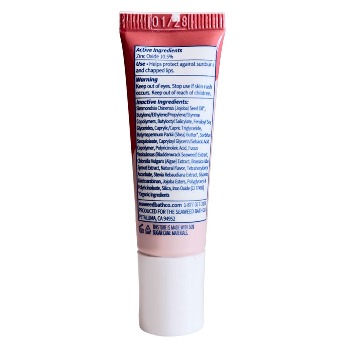 A small pink and white tube of The Seaweed Bath Co Tinted Mineral Lip Shine SPF 20, featuring text on the back listing active ingredients—including organic Atlantic seaweed and shea butter—along with warnings and manufacturer information.