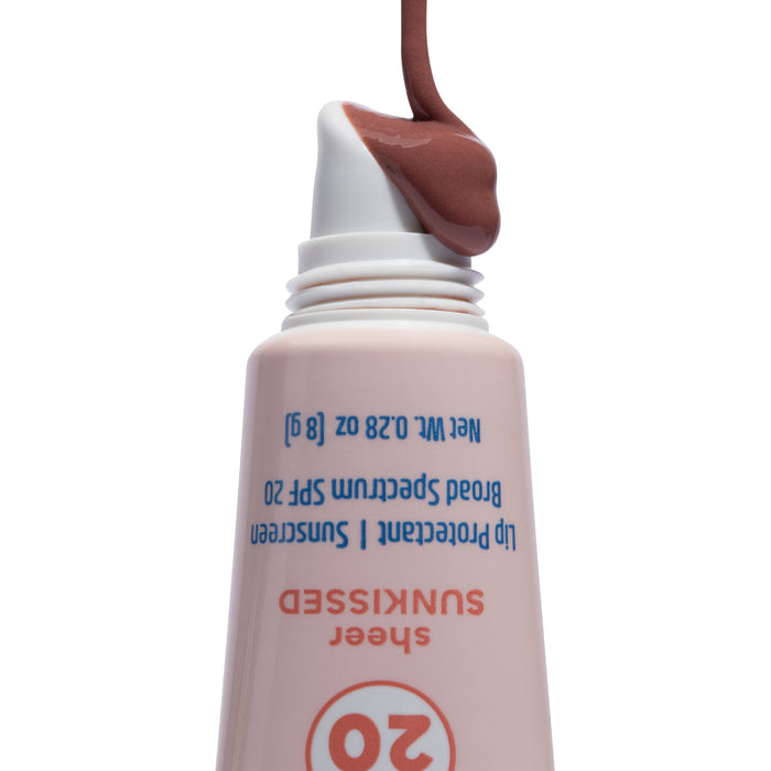 A tube of The Seaweed Bath Co Tinted Mineral Lip Shine SPF 20 is pictured upside down, with its brown-tinted formula emerging from the angled applicator tip against a white background. Enriched with nourishing shea butter, this product provides gentle yet effective lip protection.